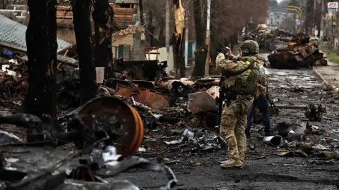 Reuters A Ukrainian soldier with a destroyed Russian tank and armoured vehicles in Bucha
