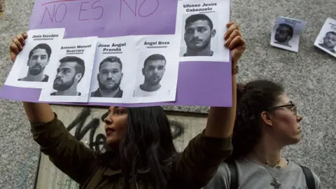 Getty Images A woman holds aloft a poster during a demonstration - on it are the photographs of the "wolf pack" with the Spanish words for "no is no"