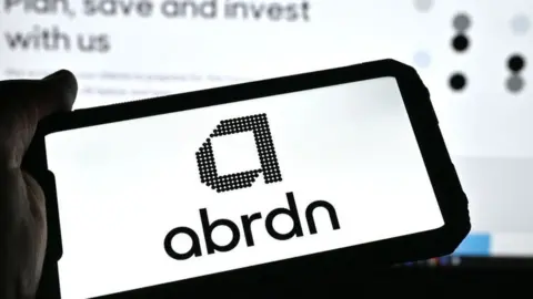 Getty Images Person holding a phone with the Abrdn logo on it