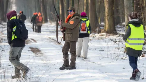 AFP A hunter with his rifle looks on as animal rights activists dressed in high-visibility yellow vests walk around him on every side.