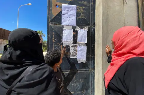 Reuters People look missing notices in the aftermath of the floods in Derna.