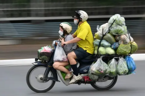 Getty Images A man riding a heavily laden motorbike with a child