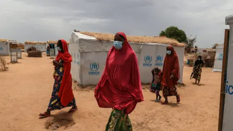 Getty Images A group of women walk through the the Bogo IDP camp during a field visit by Filippo Grandi, the United Nations High Commissioner for Refugees (UNHCR)in Maroua on April 28, 2022.