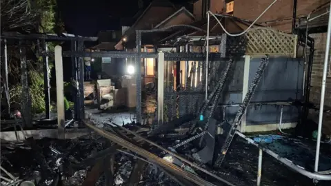 Essex Fire and Rescue Service Damaged garden in Greenwood Close, showing burnt fencing, the remains of a gazebo and damaged garden furniture