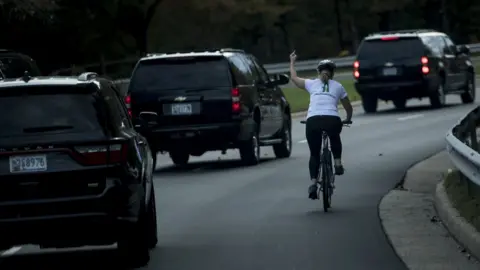 AFP/GETTY A line of motorcade cars and Juli Briskman on a cycle making a middle finger gesture