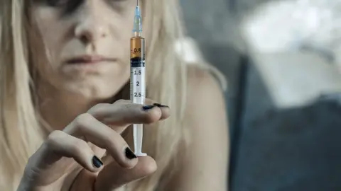 Getty Images Stock photo of drug addict holding up a syringe with a brown liquid in