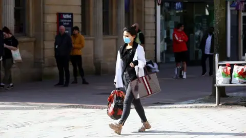 Getty Images A woman, wearing a face mask as people stand at a distance and queue to enter a bank in Cardiff in March 2020