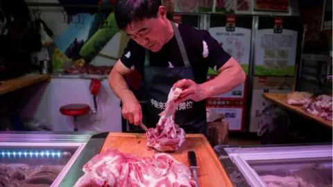 Getty Images In this picture taken on July 10, 2019 a butcher cuts a piece of porc meat at his stall at a market in Beijing