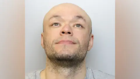 Jamie Doyle custody image. He is wearing a grey T-shirt and is looking up into the air.