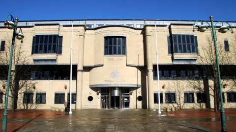 Library image showing the outside of Bradford Crown Court. It is a beige building, with three large windows on the upper level and a number of smaller square windows and a revolving door on the ground level.