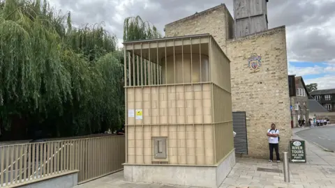 Qays Najm/BBC External image of toilets in Cambridge. It is a single-storey light beige building next to a road and a line of trees.