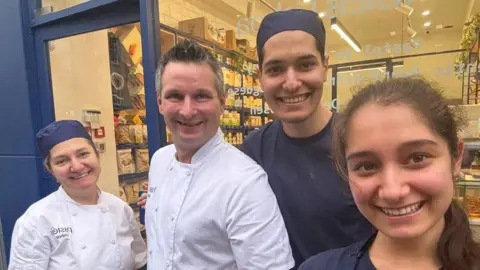 Sebastian Bacewicz wearing chef whites with some of his staff outside the Gordon Street branch of Pastéis Lisboa. There is a man and a woman wearing navy blue and a woman also wearing chef whites. 