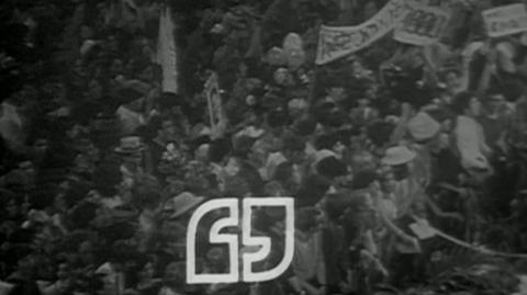 An image of a crowd holding signs, with the Talkback logo at the bottom.