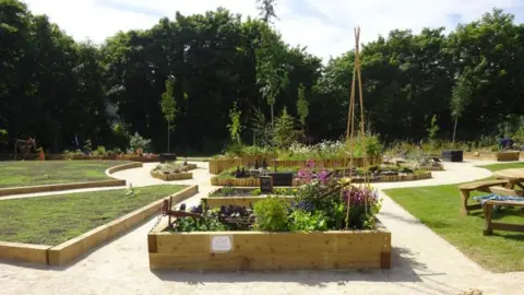 JANE PRESCOTT The garden when it opened in 2018 there are well kept raised flower beds with a circular feature in the centre and grass and benches around a path.