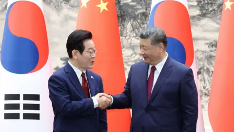 Reuters Lee Jae Myung and Xi Jinping shake hands in front of South Korea and China flags