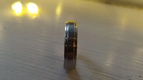 A platinum ring on a light-coloured wooden surface with a light visible in the top left of the frame