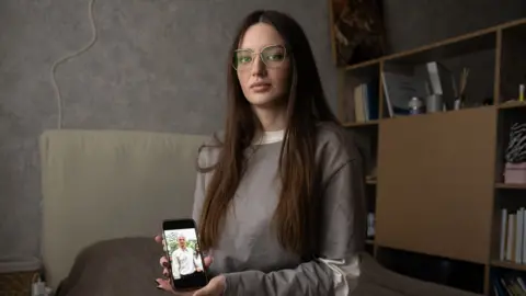 Julia Hripun sitting in her bedroom with a picture of her captive father on her iPhone