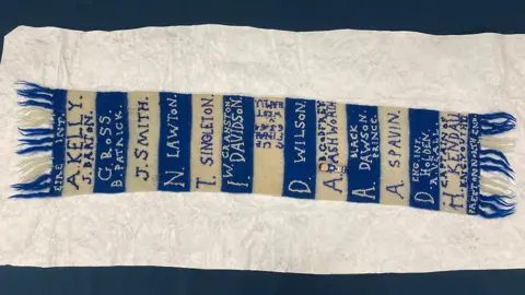 BBC/James Mountford The 1964 scarf, with blue and white stripe and fringes and names sewn over the stripes