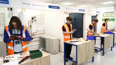 Northampton College Students wearing fluorescent jackets working with metal materials in a learning environment