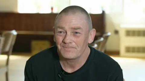 Grant Calder smiling and looking slightly off-camera, wearing a black t-shirt with short hair.
