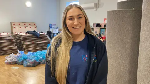 BBC lady with blonde hair smiling with blue tshirt