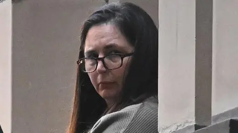 Erin Patterson, wearing glasses and with long brown hair. 