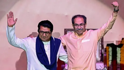 Getty Images Hindu right-wing political party chief Shiv Sena (UBT) Uddhav Thackeray (R) and his cousin and Maharashtra Navnirman Sena (MNS) president Raj Thackeray gesture as they greet the crowd upon their arrival on stage to address a joint rally against the imposition of the Hindi language in primary schools, in Mumbai on July 5, 2025.