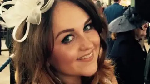 Metropolitan Police Charlotte Brown is seen smiling at the camera, wearing a white fascinator. Other wedding guests are pictured in the background. 