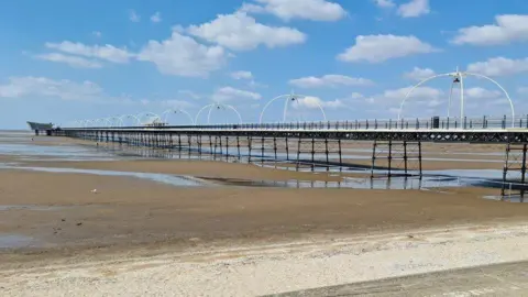 Southport's pier and beach, under a blue sky, with the tide out of sight in the distance