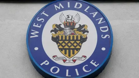 A West Midlands Police circular logo outside LLoyd House, the police HQ in Birmingham. It has a blue rim with West Midlands Police written in white and a phoenix risding from flames, Forward in Unity, it says
