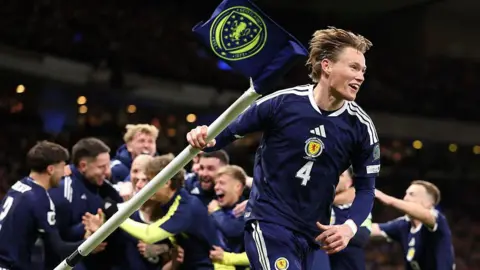 Getty Images Scotland player Scott McTominay holds up a corner flag as part of a celebration, with his team mates celebrating in the background