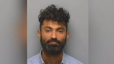 Hampshire and Isle of Wight Constabulary Mugshot of Diwan Khan, who is wearing a striped blue and shirt shirt.