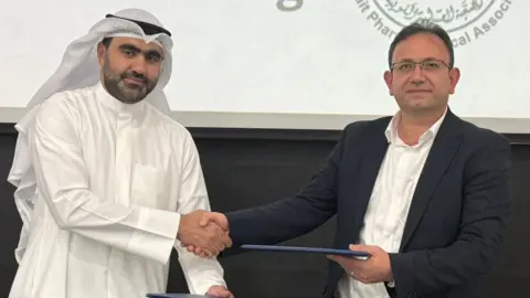 University of Reading Dr Mamoom Al Deyab is wearing a suit jacket with a white shirt, while Dr Ahmad Taqi is wearing a white ghutra and egal with white shirt. They are posing for the picture while shaking hands