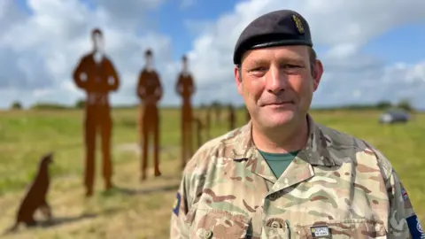 Brigadier Gavin Hatcher CBE in uniform, in front of some of the statues