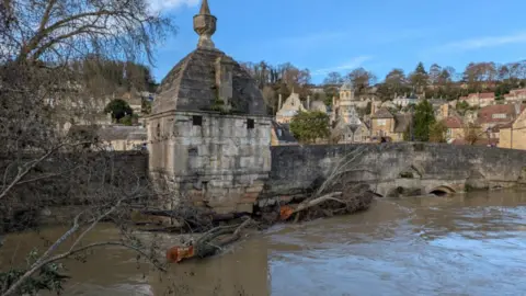 Bradford-on-Avon Town Council Town Bridge with floodwater right up to road level and a large tree trunk stuck at the parapet