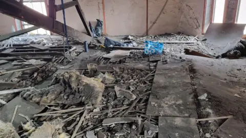 Julian Marriott A floor strewn with rubble, splintered wood and insulation material