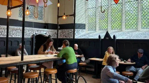 Peterborough Cathedral Diners sit at tables beneath open umbrellas in a cafe