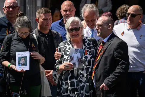 Imágenes falsas.  Víctimas y familias se encuentran afuera del Salón Central Metodista en Westminster sosteniendo fotografías de sus seres queridos.