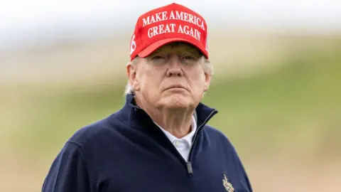 Getty Images Donald Trump playing the Ailsa course on a trip to the Turnberry resort in 2023. Trump is wearing a red baseball hat, with the 'Make America Great Again' slogan in white writing on the front and a navy blue quarter-zip jumper with a white polo shirt.