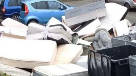 Items are piled up in the foreground. Some vehicles are behind them on the photo.
