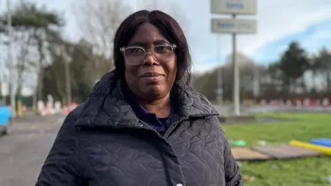 Kate Bradbrook/BBC Grace Owusu has black hair pulled back into a pony tail. She is wearing a navy quilted jacket and a blue shirt underneath.
