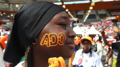 Reuters Um apoiante do RHDP (Reunião dos Houfuistas pela Democracia e Paz), o candidato presidencial Alassane Ouattara, tem as suas iniciais pintadas no rosto.