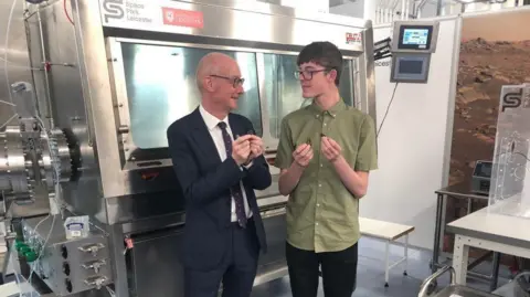 A scientist gives a demonstration about space rocks in a room filled with shiny space tech
