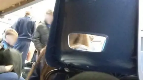 Supplied This image, taken from beneath a desk, shows children gathered in a classroom. A chair is in the foreground and blocks part of the picture. The children's faces have been blurred.