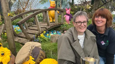 Two women sit in a highly-designed garden next to prop honey pots with a bridge in the background and model Winnie the Poo and Piglet characters.