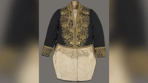 Historic Royal Palaces A black top half with gold embroidery and silky looking gold bottom half of what resembles a long suit jacket. 