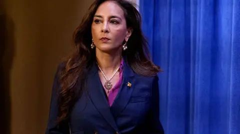 Getty Images Assistant Attorney General Harmeet Dhillon, of the Justice Department's Civil Rights Division, walks into a press conference. A blue velvet curtain serves as a backdrop.