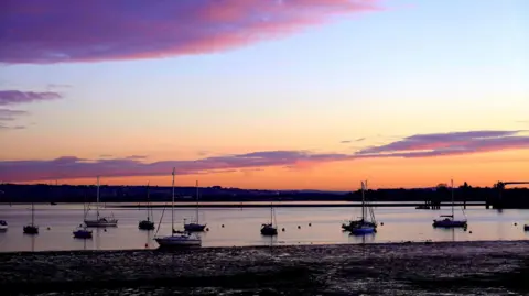BBC Weather Watcher Alison Treacher Water line at Gosport with numerous small sailing boats and a orange and purple sky during sunrise.