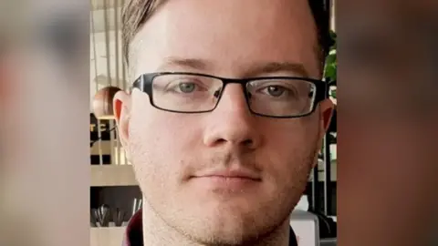 Close up image of Cameron Devlin. He has short brown hair and is wearing glasses.