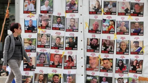 EPA A woman walking past a display of Israeli hostage posters